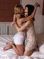 Gagged with a double ballgag, barefoot Dolly and Jessica, tied kneeling face to face, wiggles on the bed
