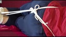 Lucy tied and gagged with ropes and a cloth gag on a sofa wearing a blue/red rainwear combination (Video)