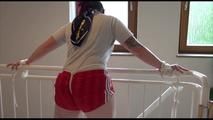 Jill tied and gagged on a stairrail wearing a sexy shiny red shorts with shadow stripes and a top (Video)