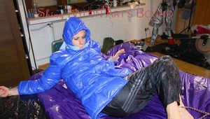 Pia tied, gagged and hooded with cuffs and chains on a bed wearing a sexy black rain pants and a blue down jacket (Pics)