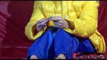 Sonja wearing a blue rain pants and a yellow PAMY down jacket while bonding herself an the sofa (Video)