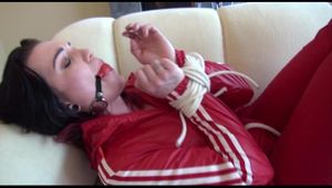 Jill tied, gagged and hooded on a white sofa wearing a sexy shiny red nylon shorts and a red rainjacket (Video)