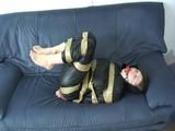 Katharina tied and gagged with tape on a sofa wearing a shiny black nylon rainsuit (Video)