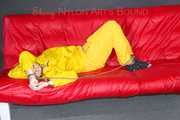 MARA ties, gagges and hoodes herself with cuffs and a ballgag on a sofa wearing sexy yellow rainwear (Pics)