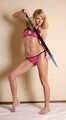 Dolly: blonde barefoot girl, wearing pink bikini, poses with the replica of a medieval sword, and then poses with a leather-steel cuffs on her hands and feet