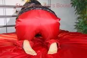 Sonja tied and gagged with a pillory on bed wearing a sexy red rain pants and a black down jacket (Pics)