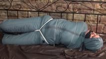 Mara tied, gagged and hooded on bed in a cellar wearing a shiny blue/grey downwear (Video)