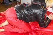 Sonja tied and gagged with a pillory on bed wearing a sexy red rain pants and a black down jacket (Pics)