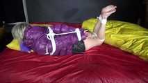 Watching sexy Sonnja wearing a black shiny nylon down skirt and a purple downjacket being tied and gagged with ropes and a ballgag on a bed (Video)