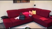 Mara tied and gagged on a sofa wearing a shiny pink down jacket and a black rain pants (Video)
