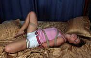 Hogtied barefoot Sharon in pink tank top and white shorts rolls and wiggles on the bed