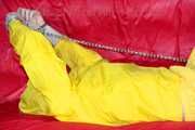 MARA ties, gagges and hoodes herself with cuffs and a ballgag on a sofa wearing sexy yellow rainwear (Pics)
