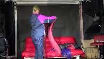Watching Pia wearing a blue/purple/pink shiny nylon rain suit folding clothes and tidying up the studio (Video)