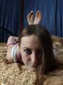 Barefoot Elly in tank-top and jeans shorts, hogtied with hemp rope, poses for the camera