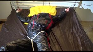 Liz tied and gagged on a bed wearing an oldschool black/red shiny nylon downwear combination (Video)