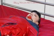 Jill tied and gagged on the bed with cable binders in a black shiny nylon pant and an red/Blue shiny rain jacket (Pics)