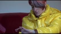 Sonja wearing a blue rain pants and a yellow PAMY down jacket while bonding herself an the sofa (Video)