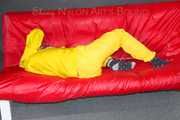 MARA ties, gagges and hoodes herself with cuffs and a ballgag on a sofa wearing sexy yellow rainwear (Pics)