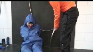 Jill in a shiny blue rainsuit tied,hooded and gagged by Simone under the shower (Video)