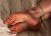 Tapegagged barefoot Grace in black bra and panties, hogtied with rope, rolls on the bed