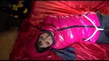 Mara tied, gagged and hooded on a bed wearing a supersexy black rain pants and a pink down jacket (Video)