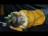 Samantha in a shiny yellow rain jacket and a shiny grey rain trowsers tied and gagged on bed (Video)