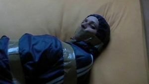 One of our archive girl tied, hooded and gagged by tape on a bed wearing shiny nylon rainwear (Video)