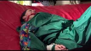 Lucy tied and gagged on a bed with red shiny nylon cloth wearing supersexy green rainwear (Video)