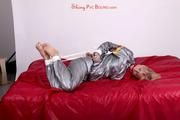 Pia tied and gagged in a shiny silver sauna suit bare feet on a bed (Pics)