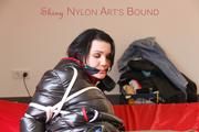 Jill tied, gagged and hooded on a bed wearing a grey rain pants and a black downjacket with closed zip for breath control play (Pics)