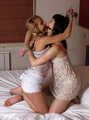 Gagged with a double ballgag, barefoot Dolly and Jessica, tied kneeling face to face, wiggles on the bed