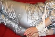 Sophie tied and gagged on the sofa wearing a shiny silver PVC sauna suit (Pics)