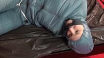 Mara tied, gagged and hooded on bed in a cellar wearing a shiny blue/grey downwear (Video)