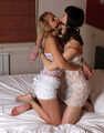Gagged with a double ballgag, barefoot Dolly and Jessica, tied kneeling face to face, wiggles on the bed