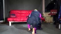 Watching Pia wearing a blue/purple/pink shiny nylon rain suit folding clothes and tidying up the studio (Video)