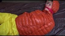 Pia tied and gagged on bed wearing a yellow rain pants and an orange downjacket (Video)