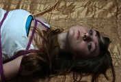 Barefoot Elly in tank-top and jeans shorts, hogtied with hemp rope, poses for the camera