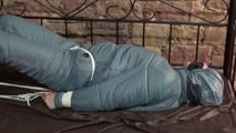 Mara tied, gagged and hooded on bed in a cellar wearing a shiny blue/grey downwear (Video)