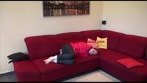 Mara tied and gagged on a sofa wearing a shiny pink down jacket and a black rain pants (Video)