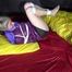 Watching sexy Sonnja wearing a black shiny nylon down skirt and a purple downjacket being tied and gagged with ropes and a ballgag on a bed (Video)