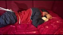 Lucy tied and gagged with ropes and a cloth gag on a sofa wearing a blue/red rainwear combination (Video)