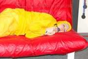MARA ties, gagges and hoodes herself with cuffs and a ballgag on a sofa wearing sexy yellow rainwear (Pics)