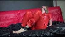 Pia wearing an supersexy red rain catsuit tied and gagged with neck ties on a sofa (Video)