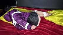 Watching sexy Sonnja wearing a black shiny nylon down skirt and a purple downjacket being tied and gagged with ropes and a ballgag on a bed (Video)