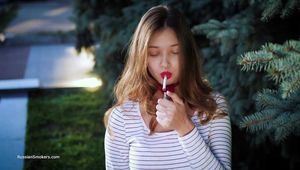 Adorable party girl Irina taking a drag on a Marlboro Red cigarette in the city park