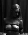 Topless barefoot Nancy in jeans shorts, hogtied with her hands in reverse prayer, wiggles on the bed