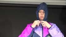 Watching Pia wearing a blue/purple/pink shiny nylon rain suit folding clothes and tidying up the studio (Video)