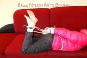 Mara tied and gagged on a red sofa wearing a sexy black rain pants and a shiny pink down jacket (Pics)