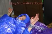 Pia tied, gagged and hooded with cuffs and chains on a bed wearing a sexy black rain pants and a blue down jacket (Pics)
