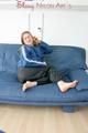 Katharina posing on a sofa wearing a blue/black shiny nylon rainwear (Pics)